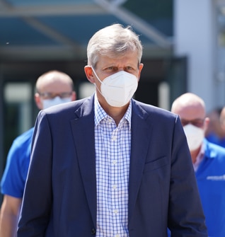 Ein Mann in einem blauen Anzug steht selbstsicher und mit einer Maske im Mittelpunkt des Bildes.